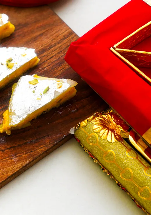 Silver-leaf barfi beside a red gift box and a gold-wrapped parcel