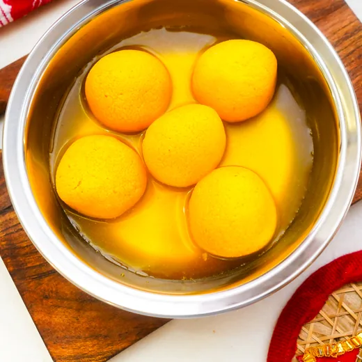 Five golden rasgulla in syrup in a steel bowl