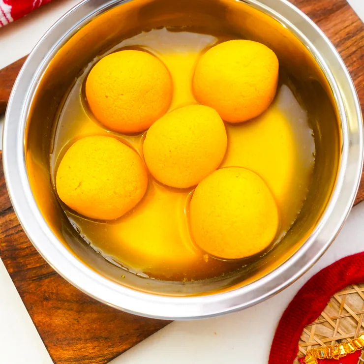 Five golden rasgulla in syrup in a steel bowl