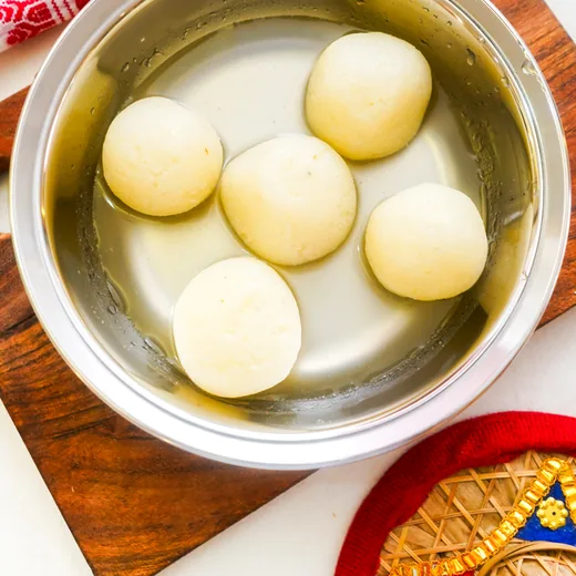 White rasgulla in light syrup in a steel bowl
