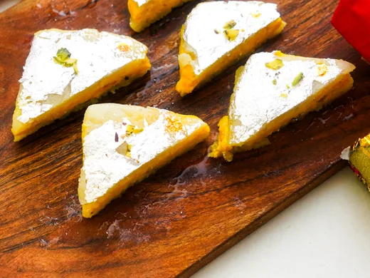 Triangular barfi pieces finished with silver leaf and pistachio on a wooden board