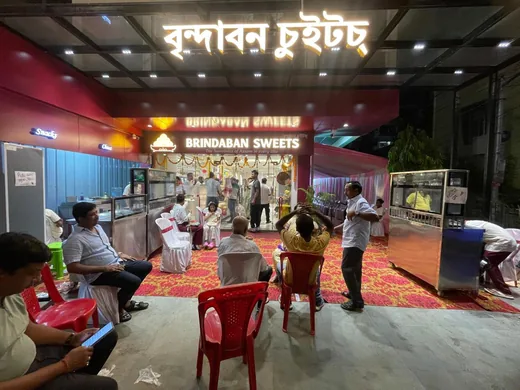 The Brindaban Sweets shopfront at night, signage lit in Assamese and English